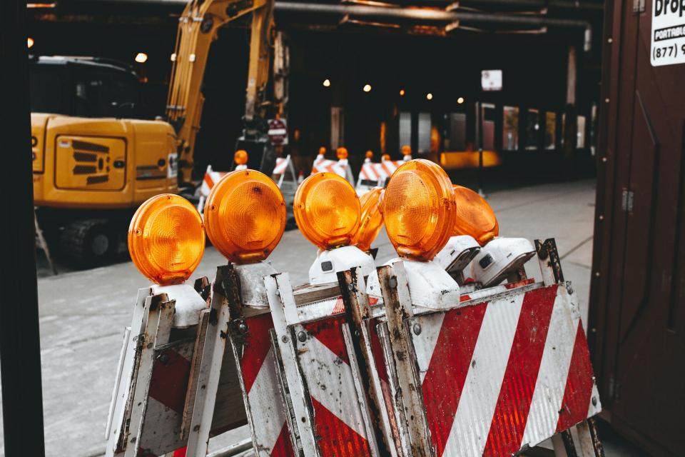 pile of caution red and white sawhorses with orange lights on top in front of construction equipment 