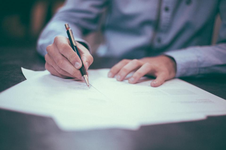 person filling out paperwork spread on table