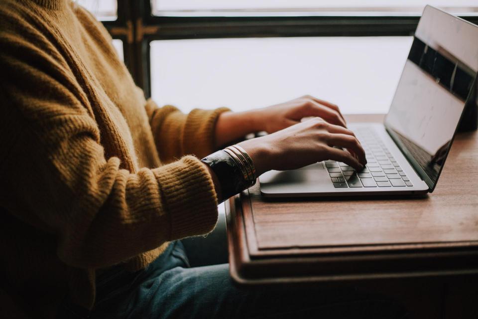 Person typing on laptop set on top of table near window